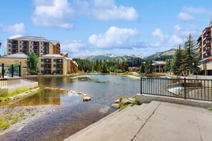 A riverside hotel with a view of mountains, a swimming pool, and a pedestrian bridge. - Walk-to-lift condo with mountain view, outdoor pool, hot tubs, gym & sauna (Breckenridge)