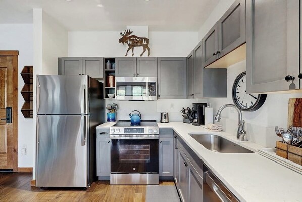A modern kitchen with stainless steel appliances, a microwave, oven, and a sink. - Walk-to-lift condo with mountain view, outdoor pool, hot tubs, gym & sauna (Breckenridge)