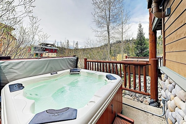 Ein Whirlpool auf einer Holzterrasse mit einer Steinmauer und einem Holzgebäude im Hintergrund.