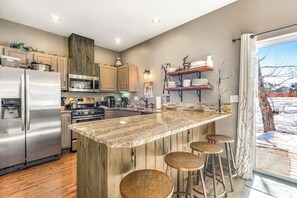 Eine moderne Küche mit Edelstahlgeräten, einer Holztheke mit Barhocker und Blick auf eine verschneite Landschaft.