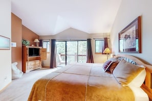 Ein Schlafzimmer mit einem großen Bett, einem Fernseher, einem Schminktisch und einem Balkon mit Vorhängen.