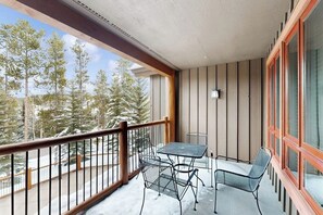 Ein Balkon mit Tisch und Stühlen, einem Geländer und Blick auf verschneite Bäume.