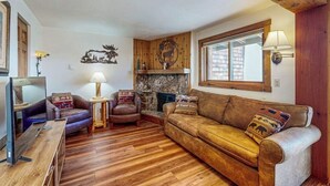 A cozy living room with a fireplace, wooden flooring, and a stone wall. - Charming Condo with Indoor Pool and Hot Tub - On Bus Line Half-Mile to Slopes (Crested Butte)