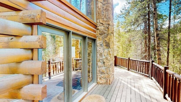 A wooden deck with glass doors leading to a deck area, surrounded by stone walls and a forested backdrop. - Serene mountainside cabin, with washer/dryer - near skiing (Almont)
