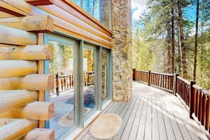 A wooden deck with glass doors leading to a deck area, surrounded by stone walls and a forested backdrop.