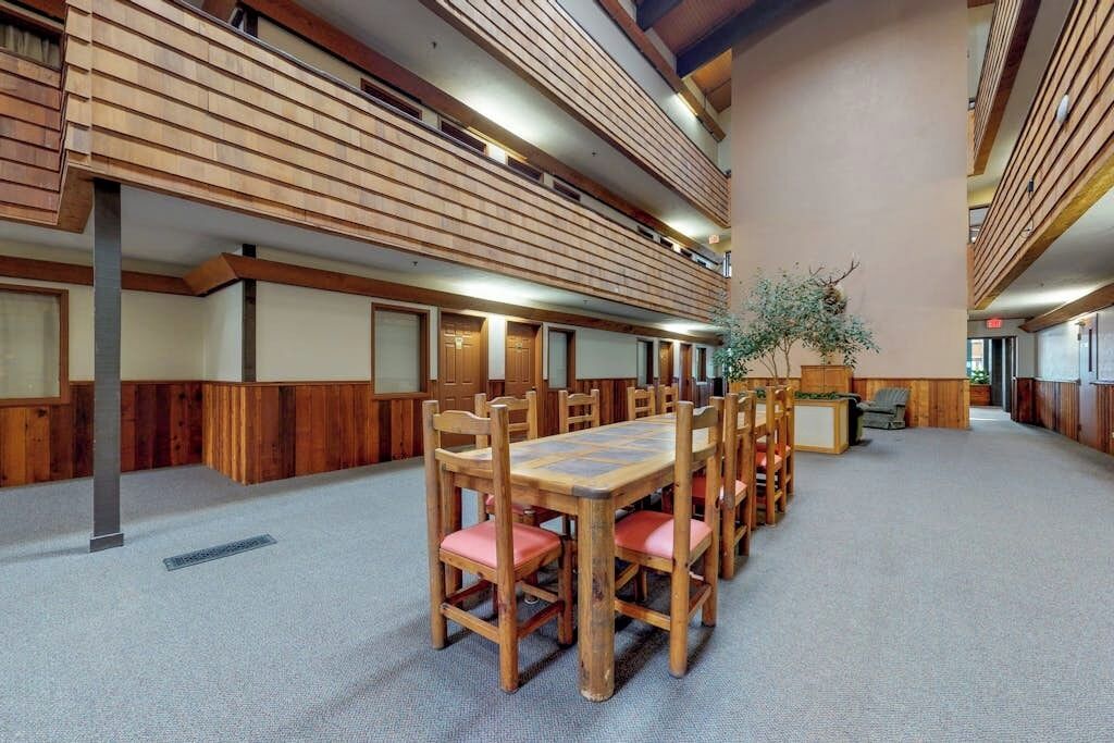 A spacious room with a long wooden table and chairs, a plant, and a wooden slatted ceiling.