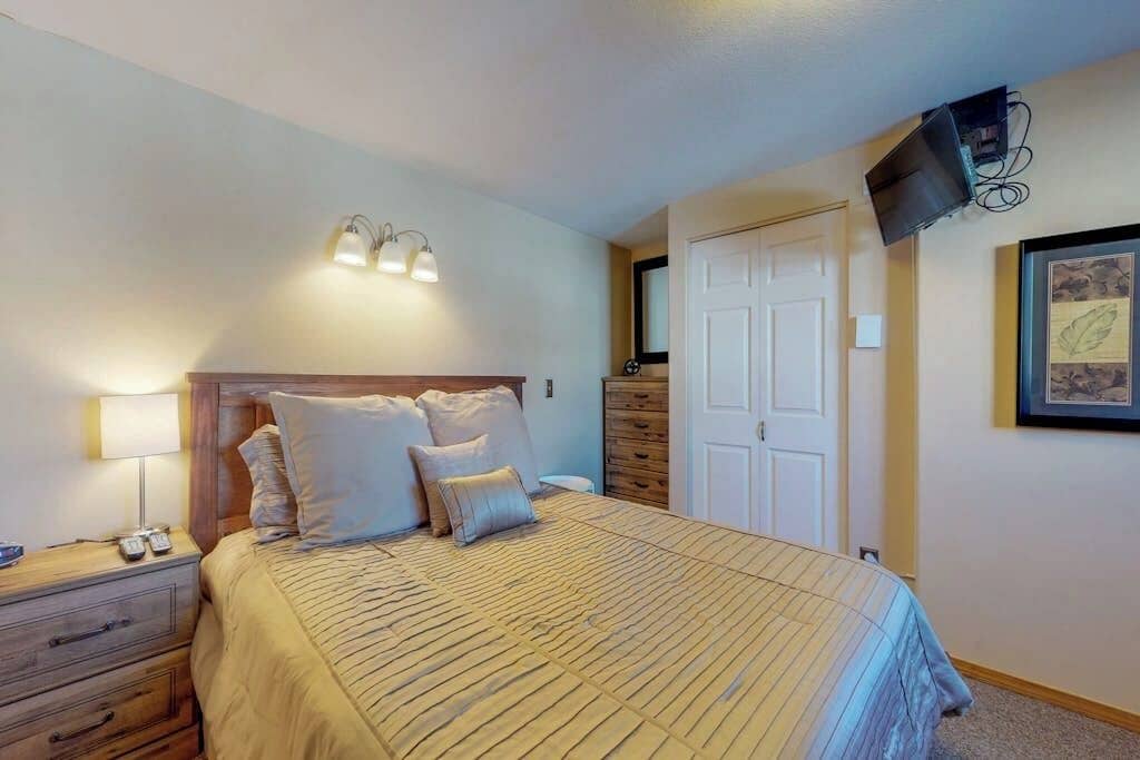 A bedroom with a bed, bedside lamps, a dresser, a TV mounted on the wall, and a door.