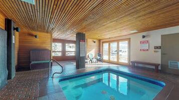 An indoor swimming pool with wooden ceiling, tiled floor, and a bench near the pool.