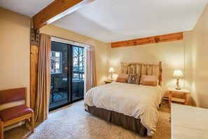 Ein Schlafzimmer mit einem großen Bett, zwei Nachttischen mit Lampen, einer Holzbank und einer Schiebetür zu einem Außenbereich.