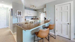 A kitchen with a central island, bar stools, a microwave, and a refrigerator. - Mountain-view condo with private deck, fireplace & hot tub (Crested Butte)
