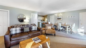 A living room with a brown leather sofa, a wooden coffee table, and a dining area with a table and chairs. - Mountain-view condo with private deck, fireplace & hot tub (Crested Butte)