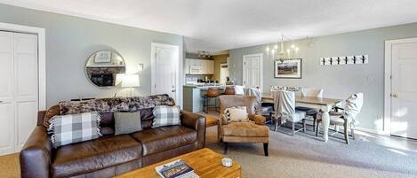 A living room with a brown leather sofa, a wooden coffee table, and a dining area with a table and chairs.