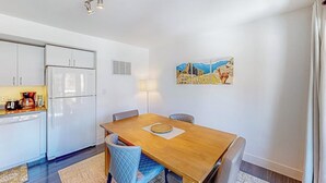 A modern kitchen with white cabinets, a refrigerator, and a coffee maker. There is a dining table with chairs and a painting on the wall. - Mountain-view condo with balcony - walk to ski lifts, near downtown Crested Butte (Crested Butte)