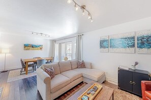 Ein Wohnzimmer mit einem beigen Sofa, einem Holztisch, einer schwarzen Kommode und Kunstwerken an den Wänden.