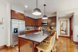 A kitchen with wooden cabinets, stainless steel appliances, a granite countertop, and pendant lighting. - Spacious condo w/ full kitchen, shared hot tubs & pool, convenient location (Breckenridge)