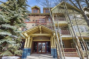 A multi-story building with a prominent entrance, balconies, and a snow-covered ground. - Spacious condo w/ full kitchen, shared hot tubs & pool, convenient location (Breckenridge)