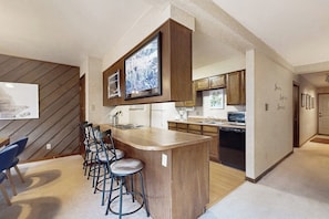 A modern kitchen with a central island, bar stools, and wooden cabinetry. - Ski condo with fireplace, washer/dryer, hot tubs - close to lifts & Main Street (Breckenridge)