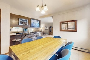 A dining area with a wooden table and blue chairs, a kitchen area with a microwave, and framed pictures on the walls. - Ski condo with fireplace, washer/dryer, hot tubs - close to lifts & Main Street (Breckenridge)