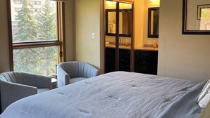 A hotel room with a large bed, a chair, a small table, and a window with a view of trees. - Rustic retreat with slopeside access, mountain views & cozy fireplace (Crested Butte)