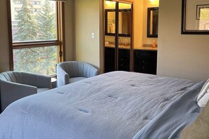 A hotel room with a large bed, a chair, a small table, and a window with a view of trees. - Rustic retreat with slopeside access, mountain views & cozy fireplace (Crested Butte)