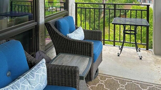 A balcony with wicker furniture, a small table, and a view of greenery. - Rustic retreat with slopeside access, mountain views & cozy fireplace (Crested Butte)