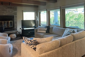 A living room with a sofa, a flat-screen TV, a fireplace, and large windows. - Rustic retreat with slopeside access, mountain views & cozy fireplace (Crested Butte)