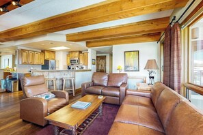 A spacious living area with leather sofas, a wooden coffee table, and a kitchen in the background. - Mountain view condo with fireplace & W/D and access to shared hot tub (Crested Butte)