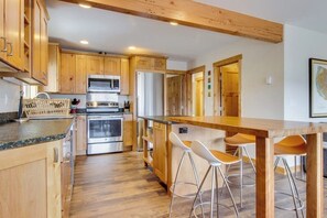 Eine Küche mit Holzausstattung, Edelstahlgeräten, einer Bar mit Hockern und einer Holzzieldecke.