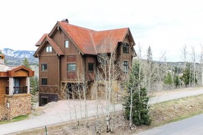 Ein mehrstöckiges Holzhaus mit geneigtem Dach, einem Steinfundament und Blick auf Berge im Hintergrund.