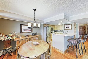 A dining area with a wooden table and chairs, a chandelier, and a kitchen in the background. - Premier Lake Dillon Condominium, 20 Min Access To 5 Resort Towns (Frisco)