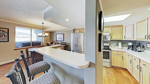 A kitchen with a bar area, wooden cabinets, a refrigerator, and a dining area with chairs. - Premier Lake Dillon Condominium, 20 Min Access To 5 Resort Towns (Frisco)