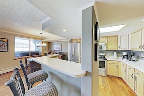 A kitchen with a bar area, wooden cabinets, a refrigerator, and a dining area with chairs. - Premier Lake Dillon Condominium, 20 Min Access To 5 Resort Towns (Frisco)