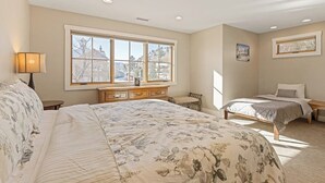 Een slaapkamer met een groot bed, een kleiner bed, een kaptafel, een raam met uitzicht en een lamp.