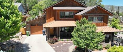 A two-story wooden house with a covered porch, a driveway, and a landscaped garden.