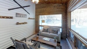 En mysig stuga med en soffa, ett soffbord och en vacker utsikt över ett snötäckt landskap genom stora fönster.