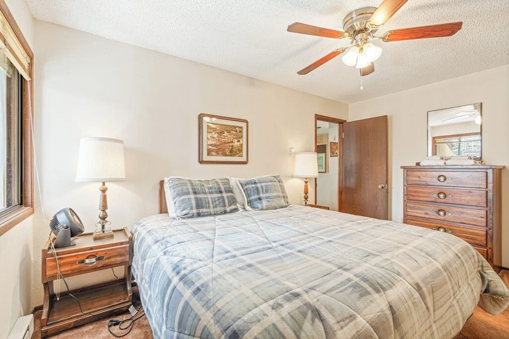 Une chambre à coucher comprenant un lit, un ventilateur de plafond, une commode, un miroir et une table de chevet avec une lampe et un ventilateur.