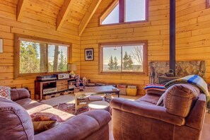 A log cabin interior with a fireplace, wooden walls, and large windows offering views of trees. - Unplugged dog-friendly getaway with tree-lined views (Durango)