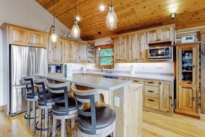 Eine Küche mit Holzausstattung, einem Edelstahlkühlschrank, einer Mikrowelle und einer Bar mit Sitzgelegenheiten.