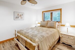 Ein Schlafzimmer mit einem hölzernen Bett, einem Nachttisch, einem Fenster mit Ausblick und einem Deckenventilator.