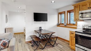 Moderni keittiö, jossa on puukalusteet, sisäänrakennettu uuni ja seinälle asennettu litteänäyttöinen televisio.
