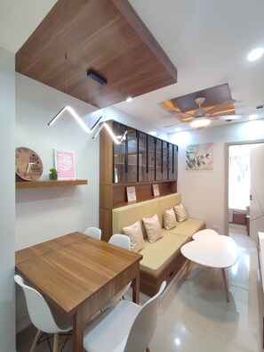 Ein modernes Wohnzimmer mit einem Holzesstisch, weißen Stühlen, einem beigen Sofa und einem Deckenventilator.