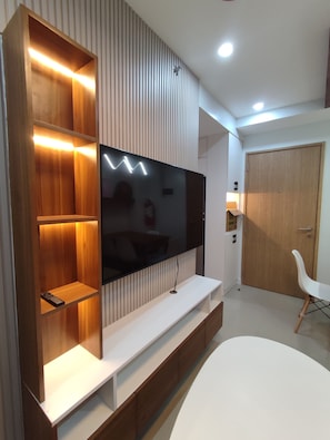 Ein modernes Wohnzimmer mit einem großen Flachbildfernseher an einer Holzwand, einem weißen Sofa und einer Holzkommode mit Regalen.