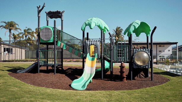Un parc infantil amb tobogans, elements per escalar i temàtica de palmeres.