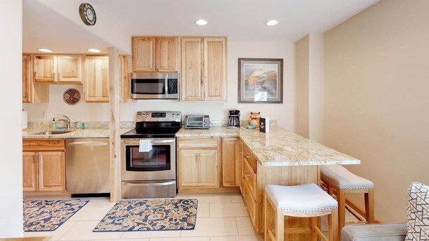 A kitchen with wooden cabinets, stainless steel appliances, a marble countertop, and a bar stool.