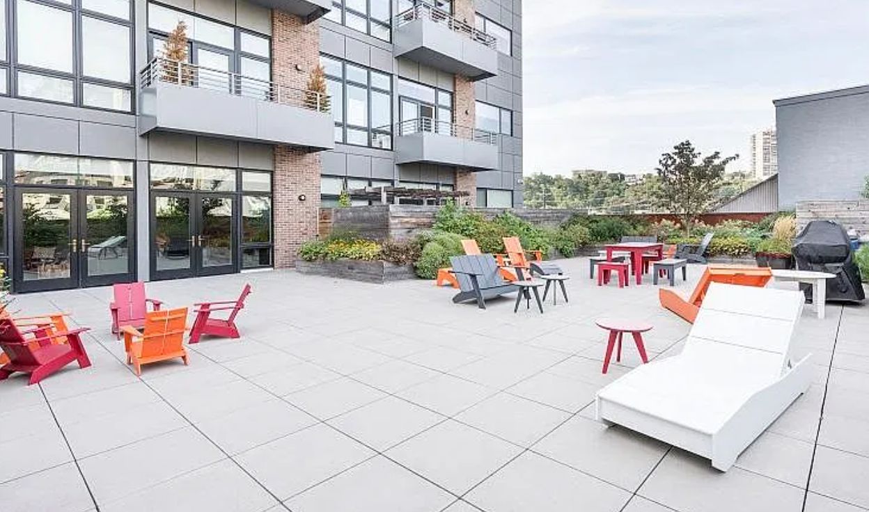 An outdoor seating area with multiple chairs and tables, a white lounge chair, and a barbecue grill.