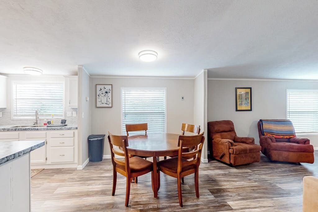 A dining area with a round table and chairs, a kitchen with white cabinets, and a living area with a sofa and armchairs.
