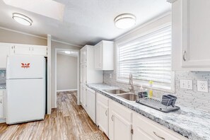 Eine Küche mit weißen Schränken, einem Kühlschrank, einer Spüle mit zwei Becken und einem Fenster mit Jalousien.