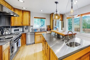 A modern kitchen with wooden cabinets, stainless steel appliances, a large island with a sink, and a view of the outdoors. - Mountain-view home in great location with walk-out apt, 2 kitchens, & W/D (Durango)