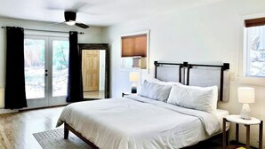 Een slaapkamer met een bed, plafondventilator, bedlampen en een raam met zonwering.