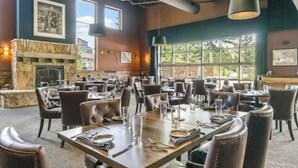 Een restaurant met meerdere tafels en stoelen, een stenen openhaard en grote ramen.